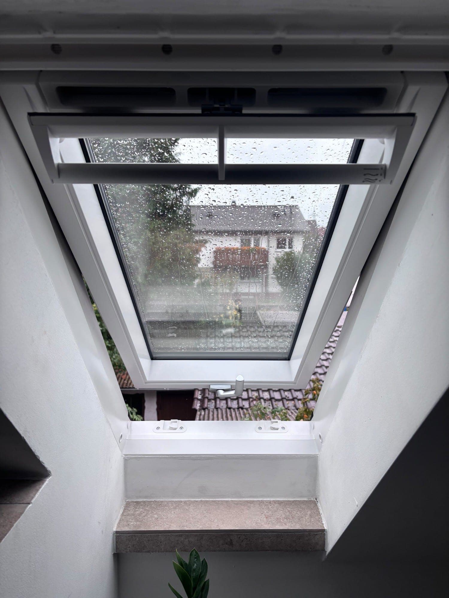 Dachfenster in Kippstellung mit Blick über die Dächer bei Regen